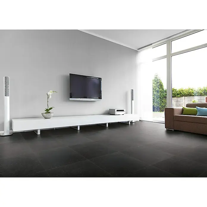 Feinsteinzeugfliese Lanzarote - 60,4 x 60,4 cm, Schwarz, Matt - Ein modernes Wohnzimmer mit dunklem Fliesenboden, einem weißen TV-Möbel, einem Flachbildfernseher und einem bequemen Sofa mit Kissen.