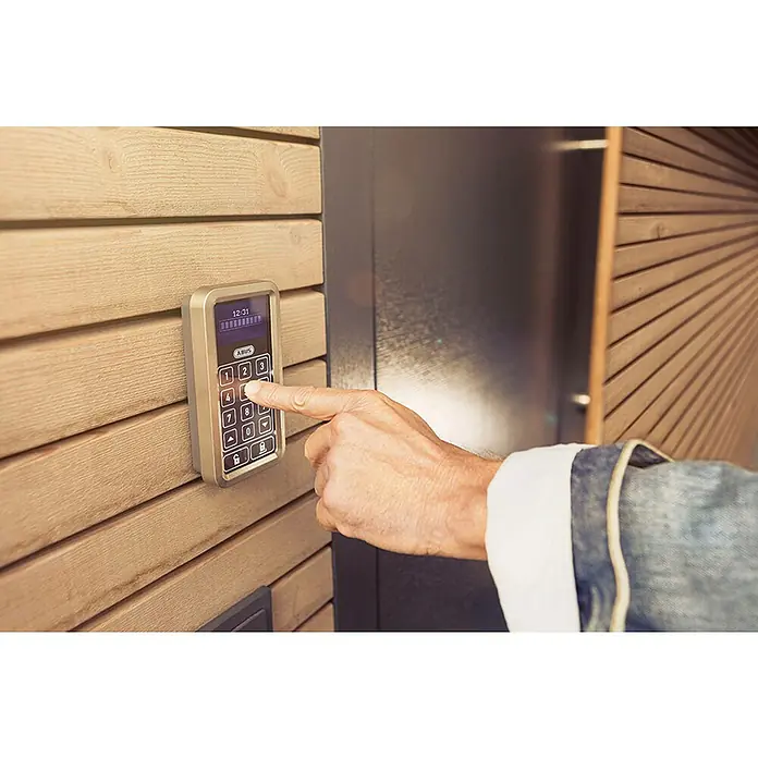 Abus Set de cerradura electrónica HomeTec Pro - 2 pzs. - Teclado ABUS: Una mano ingresa el código en un teclado ABUS montado en una pared de madera para un acceso seguro.