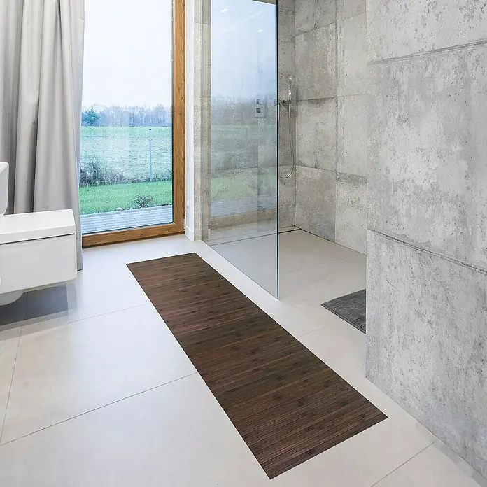 Alfombra de bambú Cool - Wengue, 200 x 50 cm - La imagen muestra una alfombra de baño de madera larga y estrecha colocada frente a una ducha y un inodoro, dando un toque natural al baño.