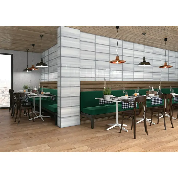 Decocer by Cinca Glow Wandfliese - 25 x 55 cm, Weiß, Glänzend - Elegantes Restaurant-Interieur mit grünen Sitzbänken, Holzboden und stilvollen Pendelleuchten, das eine einladende Atmosphäre schafft.
