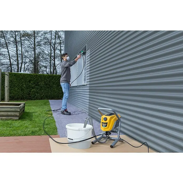 Wagner High Efficiency Airless Farbsprühsystem Control Pro 250 M - 550 W, Förderleistung: 1,25 l/min - Mann lackiert eine Fassade mit der Wagner Airless Farb-Spritzpistole, die Farbe kommt aus einem Eimer neben dem Gerät.