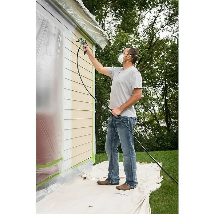 Wagner High Efficiency Airless Farbsprühsystem Control Pro 250 M - 550 W, Förderleistung: 1,25 l/min - Ein Mann streicht ein Gebäude mit einer Farbspritzpistole, um eine gleichmäßige Lackierung zu erzielen. Schutzkleidung gewährleistet Sicherheit.