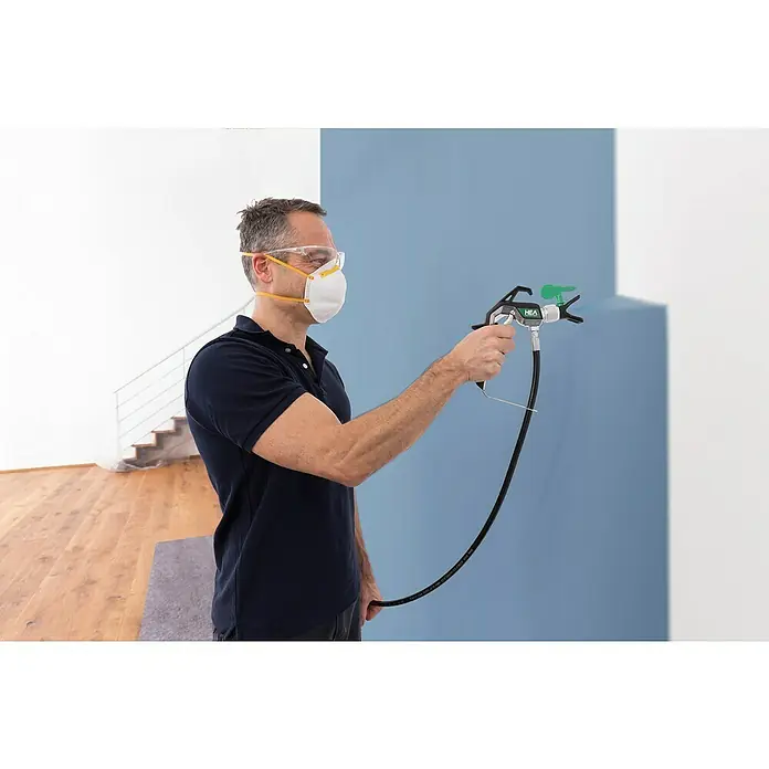 Wagner High Efficiency Airless Farbsprühsystem Control Pro 250 M - 550 W, Förderleistung: 1,25 l/min - Ein Mann mit Maske und Schutzbrille benutzt eine HEA Farbspritzpistole, um eine Wand blau zu streichen. Ideal für Malerarbeiten im Innenbereich.