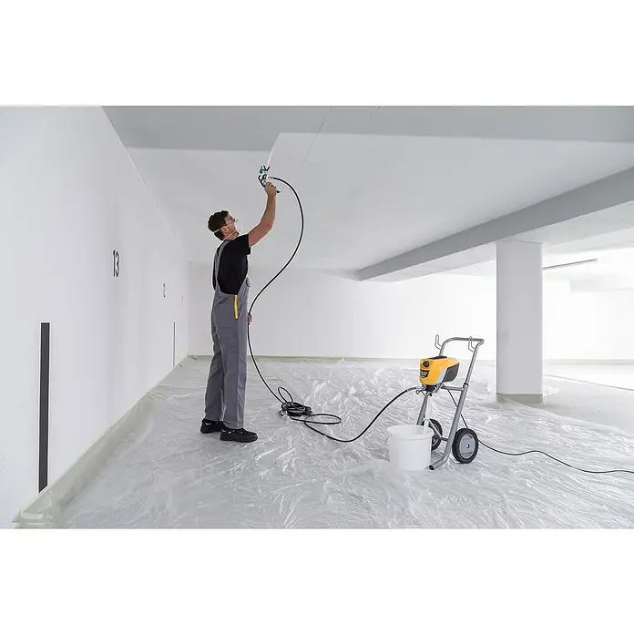 Wagner High Efficiency Airless Farbsprühsystem Control Pro 350 M Set - Leistungsaufnahme: 600 W, Förderleistung: 1,5 l/min - Ein Mann sprüht Farbe mit einer Farbspritzpistole, die mit einer gelben Wagner Farbspritzmaschine verbunden ist, um eine gleichmäßige Abdeckung zu gewährleisten.