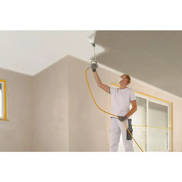 Wagner High Efficiency Airless Farbsprühsystem ProSpray 20 - Leistungsaufnahme: 900 W, Förderleistung: 1,6 l/min - Ein Mann in Arbeitskleidung benutzt eine Farbspritzpistole, um eine Zimmerdecke weiß zu streichen. Das Spritzgerät ist mit einem gelben Schlauch verbunden.
