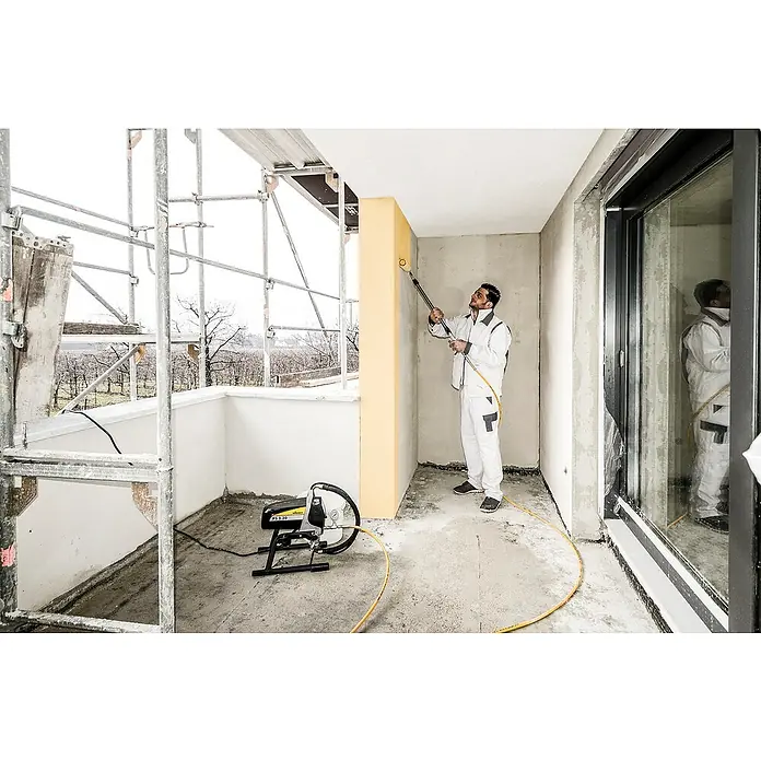 Wagner High Efficiency Airless Farbsprühsystem ProSpray 20 - Leistungsaufnahme: 900 W, Förderleistung: 1,6 l/min - Ein Maler benutzt ein Farbspritzgerät von Wagner, um einen Raum zu streichen. Das Wagner-Gerät steht auf dem Boden.