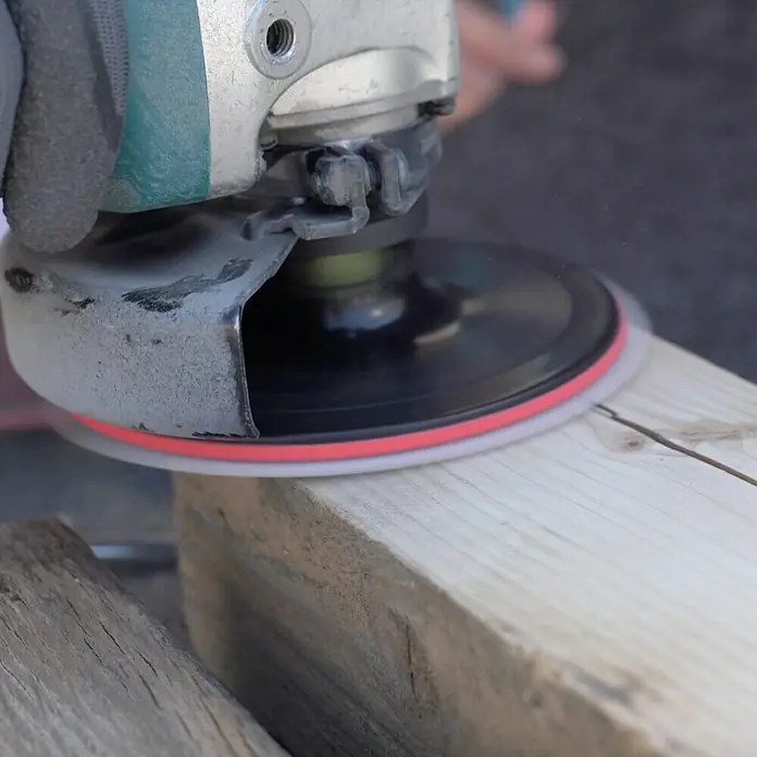 Gummischleifteller - Durchmesser: 125 mm, Durchmesser Schaft: 8 mm - Nahaufnahme eines Winkelschleifers, der zum Schleifen eines Holzstücks verwendet wird. Das Werkzeug ist im Einsatz, wodurch Staub und Späne entstehen.