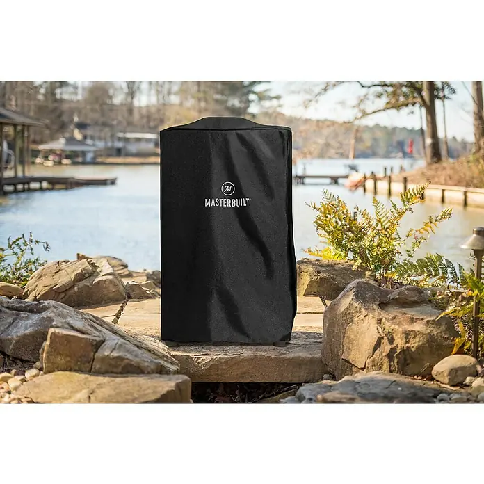 Masterbuilt Grill-Schutzhülle - Passend für: Masterbuilt Smoker Electric 40'', Polyurethan - Das Bild zeigt eine Masterbuilt-Abdeckung, die einen Grill vor den Elementen schützt, vor einem unscharfen See und Grün.