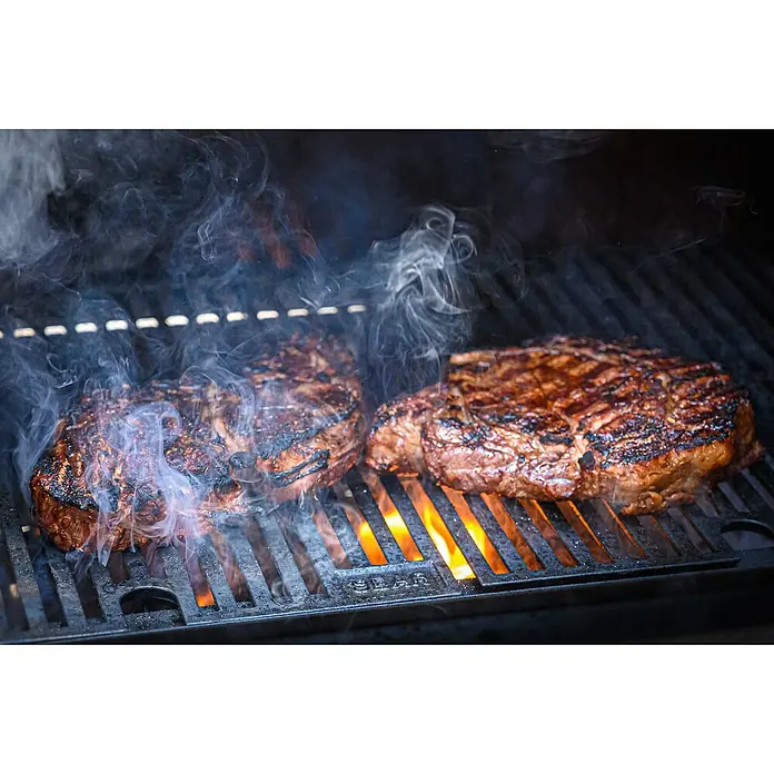 Masterbuilt Holzkohlegrill Gravity 560 Digital - Grillfläche (B x T): 56 x 38 cm, Schwarz - Zwei saftige Steaks brutzeln auf einem heißen Grill, umgeben von Rauchsäulen. Ein Fest für Fleischliebhaber!