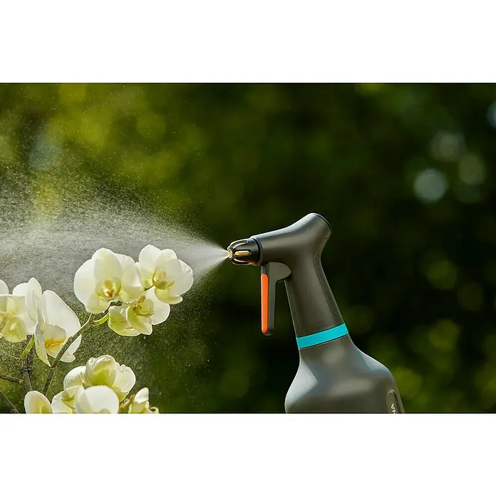 Gardena Pulverizador - 0,75 l, Plástico, Negro - Primer plano de un pulverizador de plantas Gardena en acción, rociando agua sobre orquídeas blancas, sobre un fondo verde borroso.