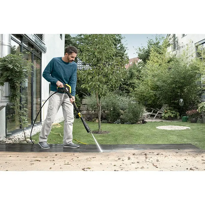 Kärcher Hidrolimpiadora de alta presión K7 Smart Control - 180 bar, 3.000 W, Capacidad de bombeo: 600 l/h - Un hombre limpia una terraza de madera con una hidrolimpiadora Kärcher, revelando el color original de la madera debajo.