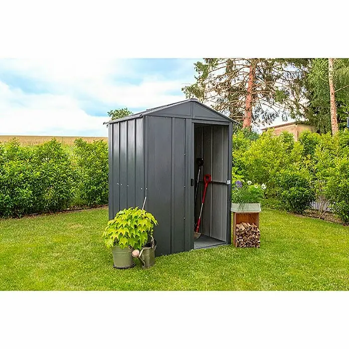 Spacemaker Gerätehaus 5x4 - Außenbreite inkl. Dachüberstand: 151 cm, Außentiefe inkl. Dachüberstand: 122 cm, Stahl, Grau - Ein graues Metallgartenhaus steht auf einem Rasen, flankiert von Büschen und einem kleinen Holzstapel. Geräte sind im Inneren sichtbar.
