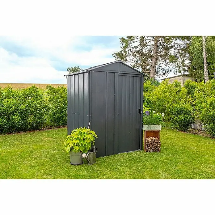 Spacemaker Gerätehaus 5x4 - Außenbreite inkl. Dachüberstand: 151 cm, Außentiefe inkl. Dachüberstand: 122 cm, Stahl, Grau - Ein graues Gartenhaus mit einem spitzen Dach, flankiert von Grünpflanzen und einem Holzstapel, steht auf einem Rasen.