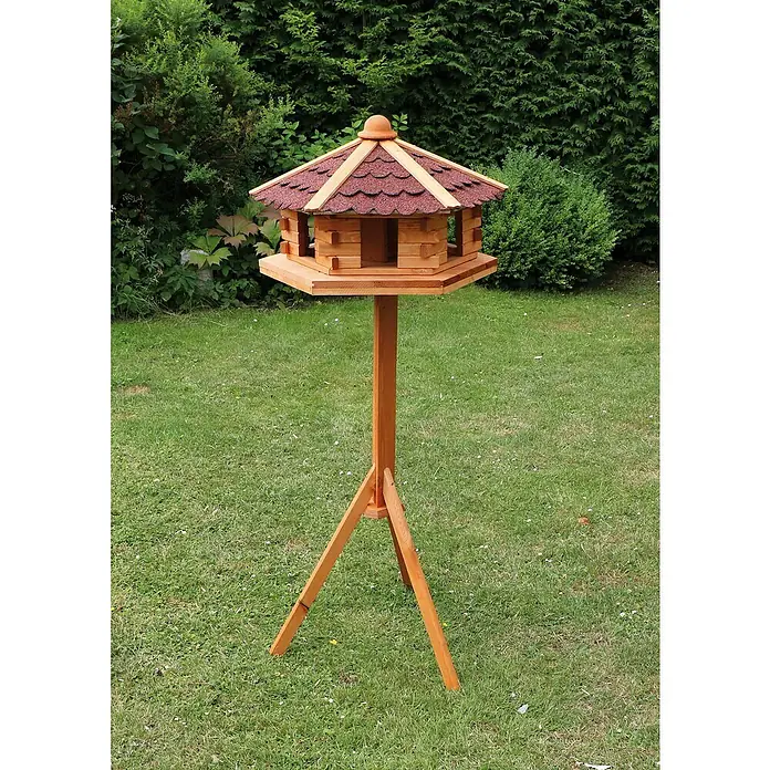 Promadino Vogelhaus Knusperhäuschen - Holz, Natur/Braun, Ausstattung: Vogelhausständer, Mit Silo - Das Foto zeigt ein hölzernes Vogelhaus mit rotem Dach, das auf einem hohen Ständer in einem Garten steht.