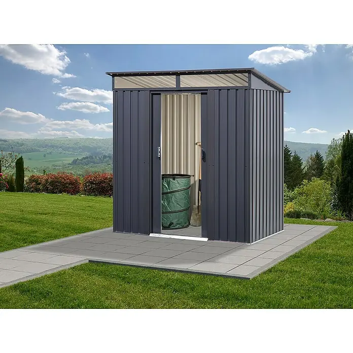 Floraworld Gerätehaus - Außenmaß inkl. Dachüberstand (B x T): 195 x 121 cm, Stahl, Anthrazit, Mit Oberlicht - Ein Metallgartenhaus mit Schiebetüren auf einer gepflasterten Fläche im Garten. Im Inneren befindet sich ein grüner Sack und eine Schaufel.