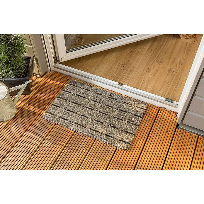 Astra Fußmatte Perfo Rips - Beige, 40 x 60 cm, 100 % Polypropylen - Die Fußmatte mit Streifenmuster vor einer Terrassentür. Der Boden ist aus Holz und es steht eine Gießkanne daneben.
