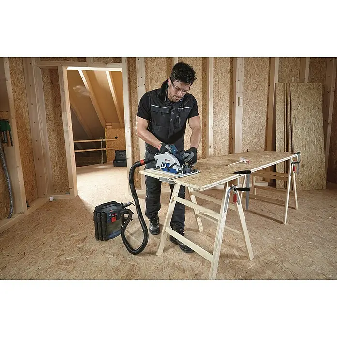 Bosch Professional AMPShare 18V Akku-Handkreissäge GKS 18V-68 GC Solo - 18 V, Ohne Akku, Durchmesser Sägeblatt: 190 mm, Leerlaufdrehzahl: 2.500 U/min - 5.000 U/min - Ein Mann schneidet mit einer Bosch Kreissäge ein Holzbrett, während ein Staubsauger den Staub absaugt.