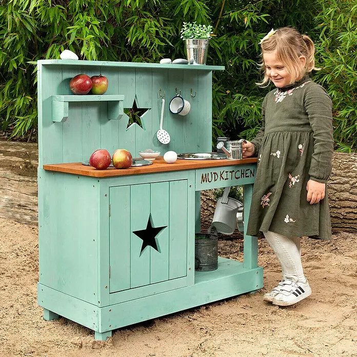 Muddy Buddy Matschküche Adventurer Star - 80 x 40 x 90 cm, Holz, Petrolblau - Ein bezauberndes Kind spielt mit einer türkisfarbenen Outdoor-Spielküche aus Holz, die mit Sternen verziert ist.