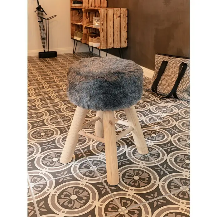 Feinsteinzeugfliese Vintage Classic25 x 25 cm, Schwarz/Grau/Weiß, Matt - Ein runder Hocker mit grauem Kunstfellbezug und hellem Holzgestell steht auf einem gemusterten Fliesenboden.