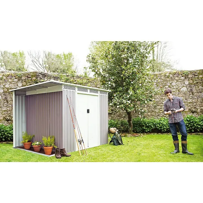 Hoggar Gerätehaus Husavik - Außenmaß inkl. Dachüberstand (B x T): 257 x 206 cm, Taupe, Stahl, 5,3 m² - Gartenhaus aus Metall mit Geräten, Pflanzen und einem Mann, der sein Werkzeug kontrolliert. Das Haus bietet Stauraum und fügt sich in den Garten ein.
