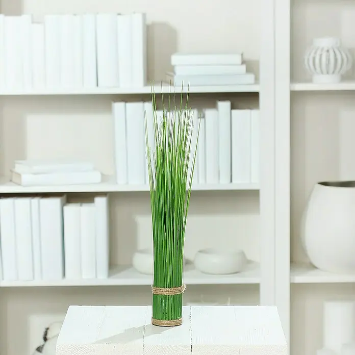 Kunstpflanze Stehgras-Bündel - Höhe: 45 cm, Kunststoff - Dekorative grüne Gräser in einem zylindrischen Topf mit Juteseil umwickelt, platziert auf einem weißen Tisch vor einem Bücherregal.