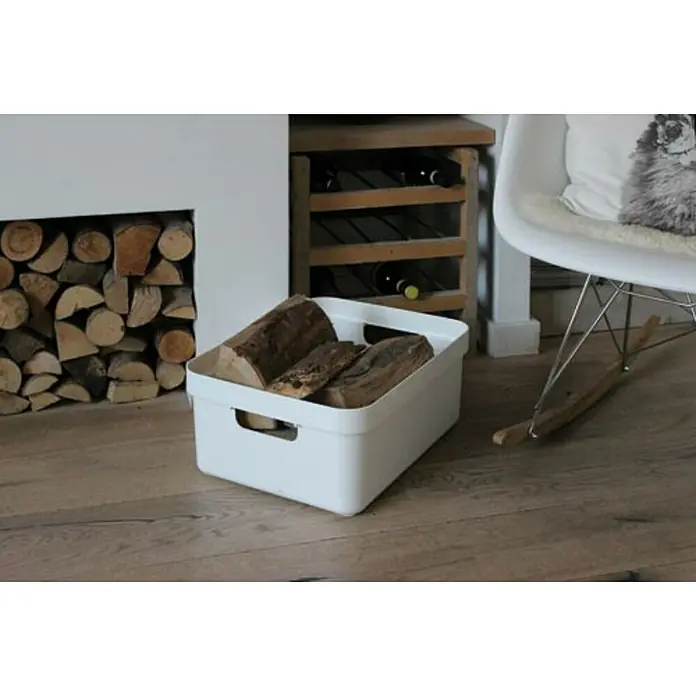 Sunware Aufbewahrungsbox Sigma Home - L x B x H: 44,5 x 34,5 x 18,3 cm, Kunststoff, Weiß - Ein weißer Behälter, gefüllt mit Holzscheiten, steht auf einem Holzboden, neben einem Regal und einem Stuhl. Praktische Holzaufbewahrung.