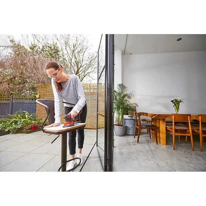 Black+Decker 18V PowerConnect Lijadora delta de batería BDCDS18N-XJ - 18 V, Iones de litio, Sin batería - Mujer lijando un taburete de bar con una lijadora BLACK+DECKER en un patio que se abre al salón.