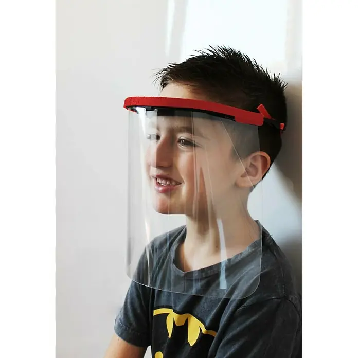 Tayg Pantalla protectora infantil - Plástico, Reutilizable - Un niño lleva un protector facial rojo que protege la cara de influencias externas. La visera es clara y sin distorsiones.