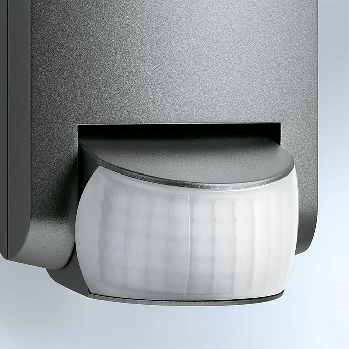 Steinel Bewegungsmelder IS 130-2 anthrazit - Reichweite Sensor: 12 m, Anthrazit, Erfassungswinkel Sensor: 130 °, L x B x H: 8,7 x 7,8 x 8,4 cm - Nahaufnahme eines grauen Bewegungsmelders mit weißer Linse vor einem neutralen Hintergrund.