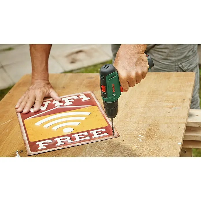 Bosch Power for All 12V Akku-Bohrschrauber EasyDrill 1200 - 12 V, Ohne Akku - Ein Mann bohrt mit einem grünen Bosch Akku-Bohrer Löcher in ein Schild mit der Aufschrift "WiFi Free".