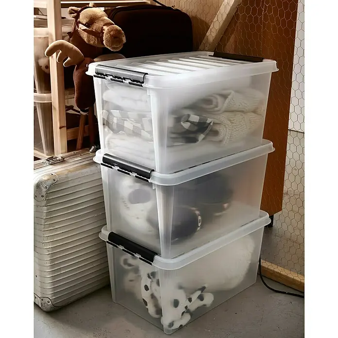 SmartStore Aufbewahrungsbox Classic 46 - L x B x H: 60 x 40 x 31 cm, Kunststoff, Transparent - Drei transparente Aufbewahrungsboxen mit schwarzen Verschlüssen, gestapelt, gefüllt mit Kleidung und Spielzeug.