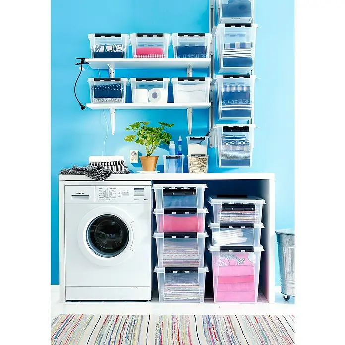 SmartStore Aufbewahrungsbox Classic 25 - L x B x H: 40 x 30 x 32 cm, Kunststoff, Transparent - Aufbewahrungslösung mit durchsichtigen Behältern mit Deckel für Kleidung im Waschraum mit blau gestrichenen Wänden und einer Waschmaschine.