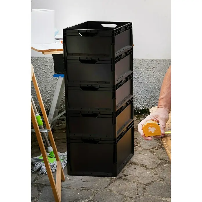 Surplus Systems Eurobox - L x B x H: 40 x 30 x 22 cm, Kunststoff, Schwarz - Ein Stapel schwarzer, faltbarer Transportkisten steht im Raum, daneben eine Person mit einem gelben Messband.