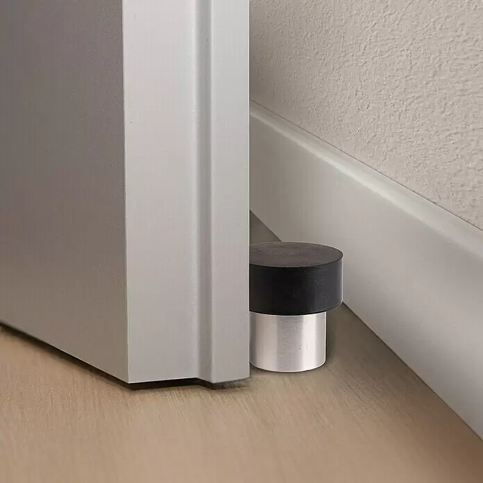 Bodentürstopper - Ø x H: 25 x 35 mm - Ein schwarzer und silberner Türstopper verhindert, dass eine hellgraue Tür die Wand trifft. Er steht auf einem Holzfußboden vor einer weißen Fußleiste.