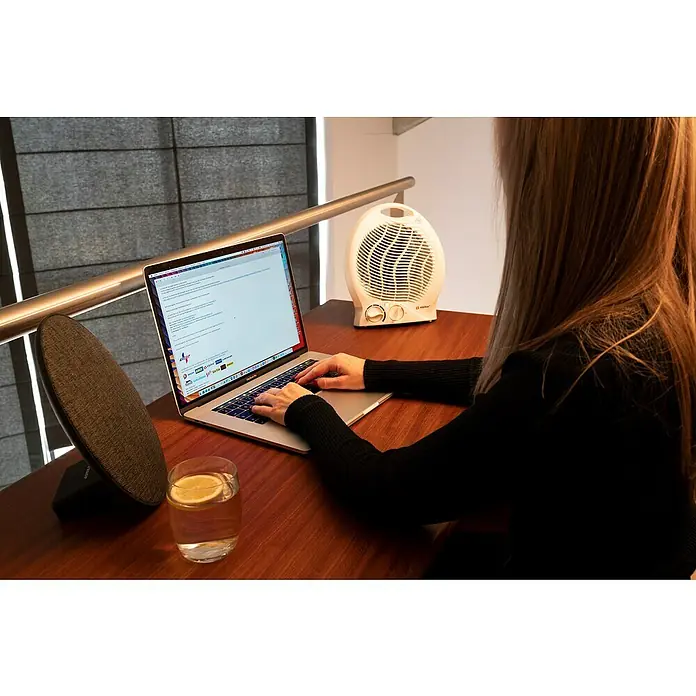 Calefactor de aire Alpina - 1.000 W - 2.000 W, Blanco - Primer plano de una mujer trabajando en su computadora portátil, con un calentador blanco al fondo y un vaso de agua con limón en la mesa.