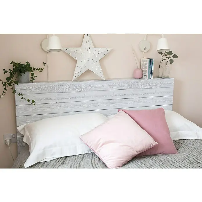 D-c-fix Holzoptikfolie Shabby Wood - 200 x 45 cm, Weiß, Selbstklebend - Nahaufnahme eines Bettes mit einem Holzkopfende, weißen Kissen und rosa Zierkissen, das eine gemütliche und einladende Schlafumgebung zeigt.
