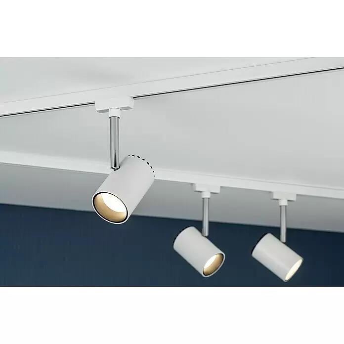 Paulmann URail LED-Leuchte Shine - L x B x H: 180 x 59 x 90 mm, 5 W, Weiß - Drei weiße zylindrische Stromschienenstrahler mit Chromstangen beleuchten eine blaue Wand, montiert an einer weißen Deckenschiene.