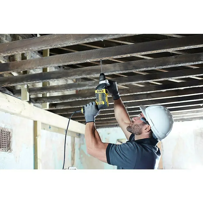 Stanley FatMax Taladro percutor FMEH750K-QS con maletín - 750 W, Portabrocas de sujeción rápida - Un trabajador de la construcción utiliza un taladro amarillo Stanley Fatmax para perforar un techo, con casco y guantes por seguridad.
