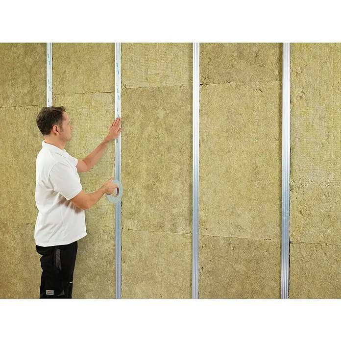Siga Doppelseitiges Klebeband Twinet - 50 m x 20 mm - Ein Mann befestigt mit Klebeband eine Metallschiene an einer mit Steinwolle gedämmten Wand. Fachgerechte Dämmung für ein energieeffizientes Haus.