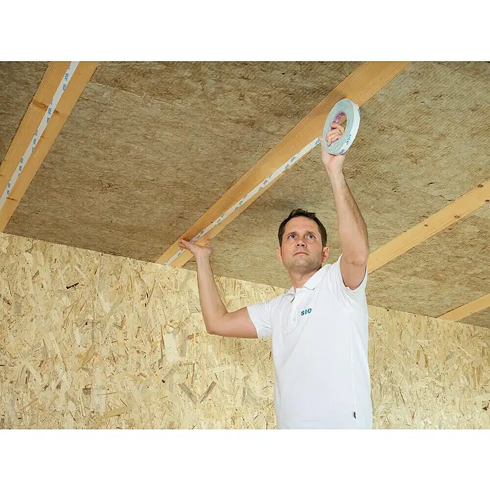 Siga Doppelseitiges Klebeband Twinet - 50 m x 20 mm - Ein Mann befestigt Klebeband an Holzbalken an einer Decke, um die SIGA-Dichtheit zu gewährleisten. Verarbeitung von Bauprodukten.