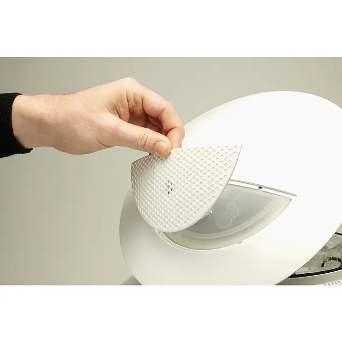 biOrb Terrarium AIR - Ø x H: 51,2 x 57,8 cm, 60 l, Weiß, Kunststoff - Eine Hand setzt einen weißen, perforierten Filter in einen runden Luftbefeuchter. Der Filter ist halbmondförmig und weist ein Lochmuster auf.