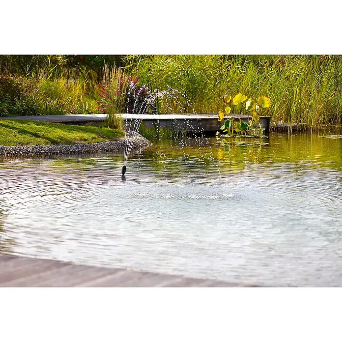Oase Unterwasserfilter Filtral UVC 3000 - 9 W, Teichgröße: 3 m³ - Ein Springbrunnen sprüht Wasser in einem ruhigen Teich, umgeben von üppiger Vegetation und einem hölzernen Gehweg.