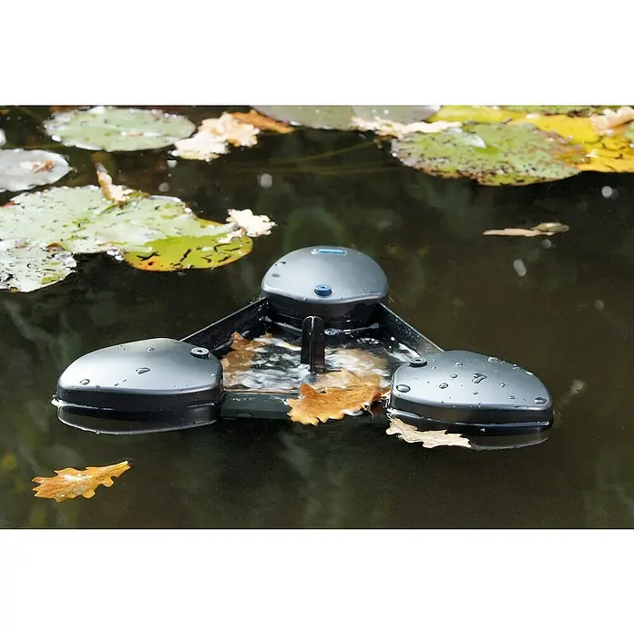 Oase Skimmer SwimSkim 25 - Leistungsaufnahme: 40 W, Fördermenge pro Std.: 2.500 l - Nahaufnahme eines automatischen Poolreinigers, der auf dem Wasser treibt, umgeben von Seerosenblättern und heruntergefallenen Blättern.