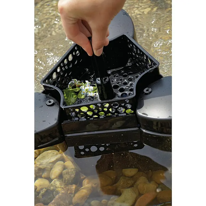 Oase Skimmer SwimSkim 25 - Leistungsaufnahme: 40 W, Fördermenge pro Std.: 2.500 l - Nahaufnahme einer schwarzen schwimmenden Pflanzinsel mit einer Hand, die Blumen in sie legt, im Wasser.