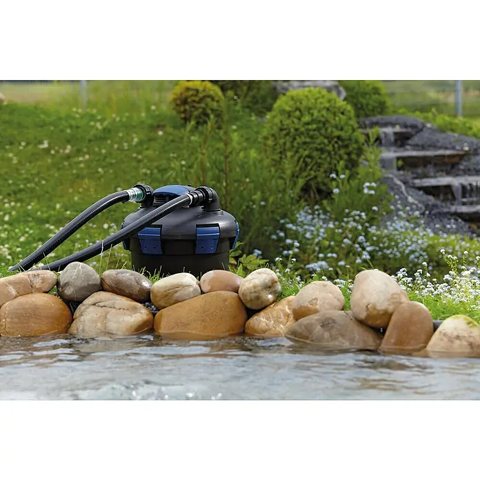 Oase Druckfilter BioPress Set 6000 - 40 W, Teichgröße: 6 m³ - Ein Teichfilter, der an einem Teichrand mit Steinen platziert ist, sorgt für klares Wasser und eine saubere Umgebung im Gartenteich.