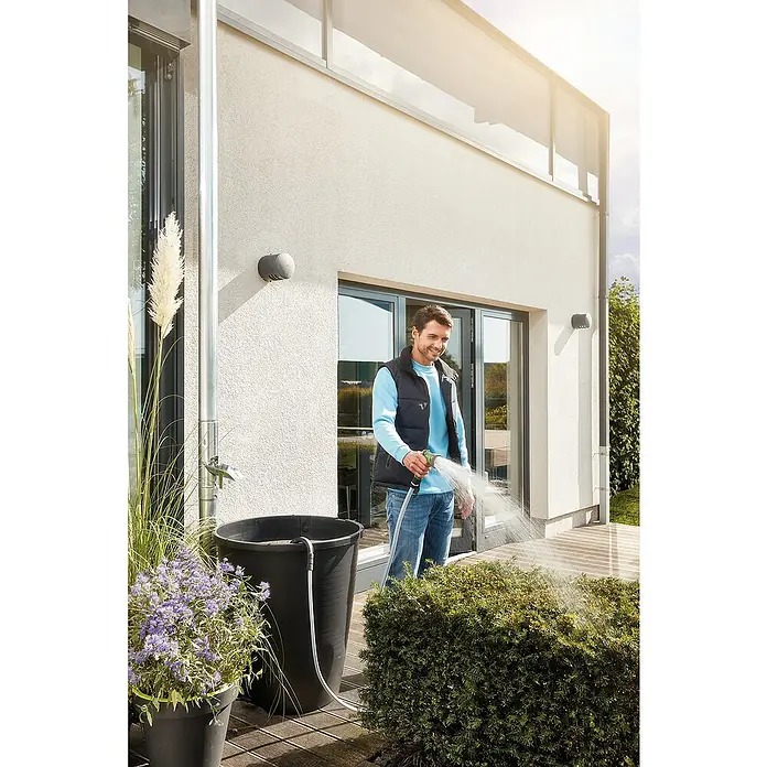 Oase ProMax Rain Regenfasspumpe ProMax Rain - 370 W, 4.000 l/h - Ein Mann bewässert einen Garten mit einer Regentonne. Nachhaltige Gartenarbeit mit Regenwassernutzung.