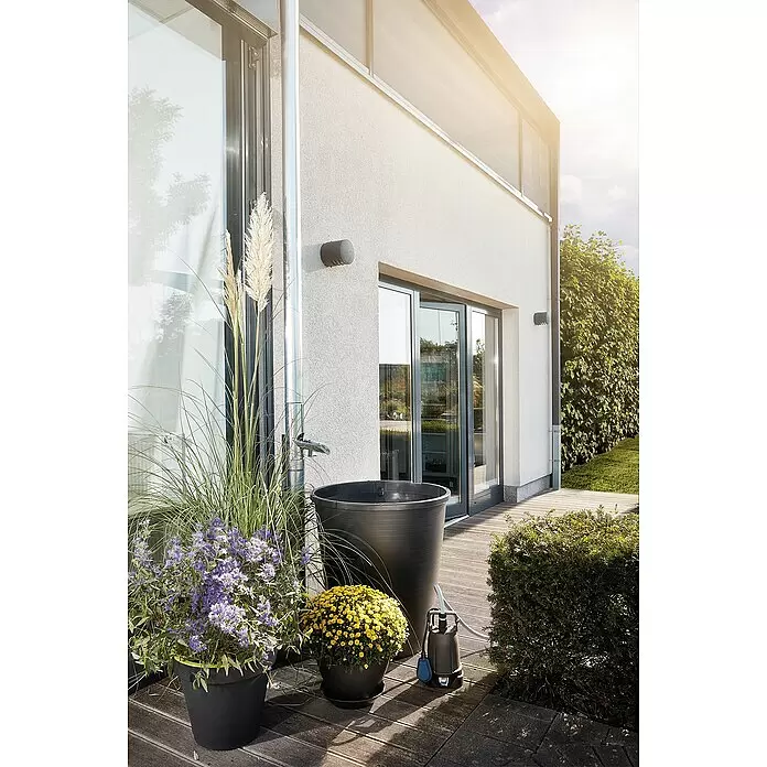 Oase ProMax Rain Regenfasspumpe ProMax Rain - 370 W, 4.000 l/h - Eine dunkelgraue Tauchpumpe mit hellblauem Schwimmer und Schlauchanschluss, neben einer schwarzen Regentonne auf einer Holzterrasse.