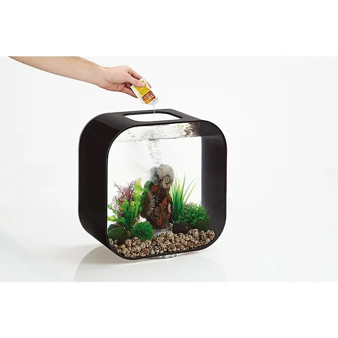 biOrb Aquarien Service-Kit - 10 -tlg., Passend für: biOrb Aquarien - Ein schwarzes, würfelförmiges Aquarium wird mit einer Flüssigkeit aus einer gelben Flasche befüllt.