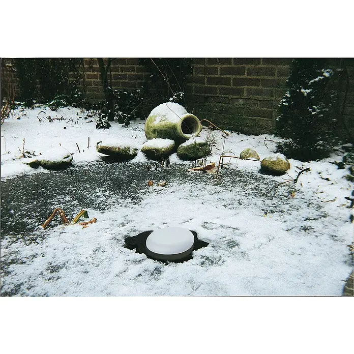 Pontec Eisfreihalter PondoPolar - Polystyrol, Rund - Winterliche Szene mit einem schneebedeckten Deckel eines Wasserbrunnens, umgeben von Steinen und einem Tongefäß.