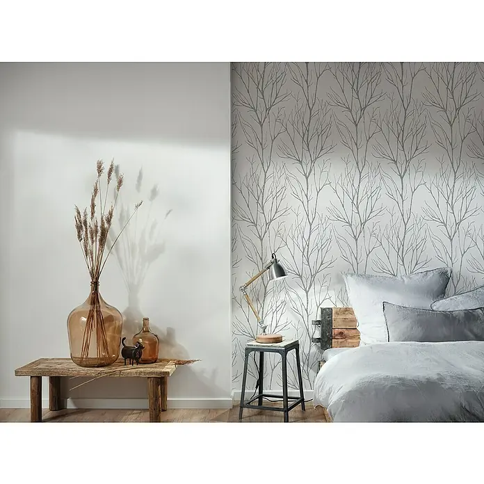 A.S. Création Papel pintado de vellón Ramas Árbol - Blanco/Negro, Gráfico, 10,05 x 0,53 m - Dormitorio rústico con un gran jarrón de vidrio con decoración, una mesa y una cama frente a una pared empapelada.